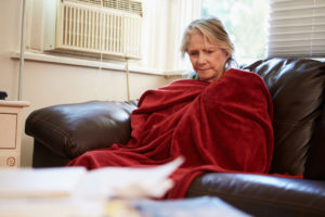 Senior Woman Trying To Keep Warm Under Blanket At Home Looking Off Camera